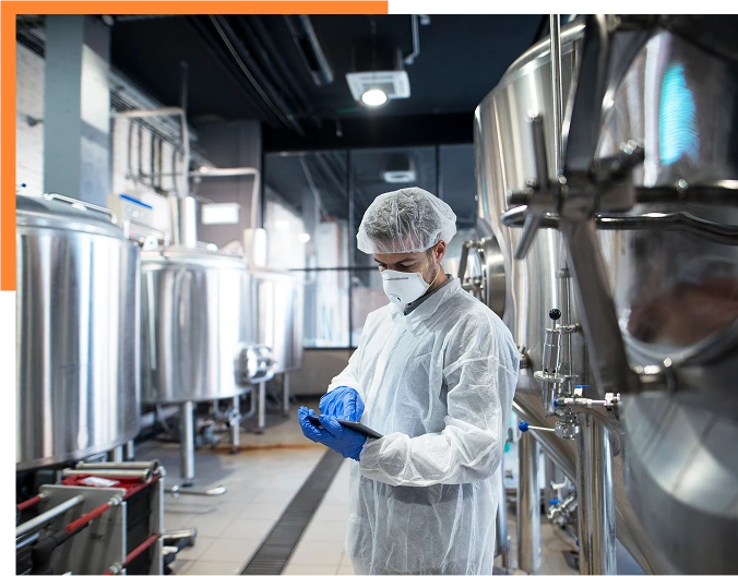 Factory worker in white protective uniform with hairnet and mask standing by industrial machine