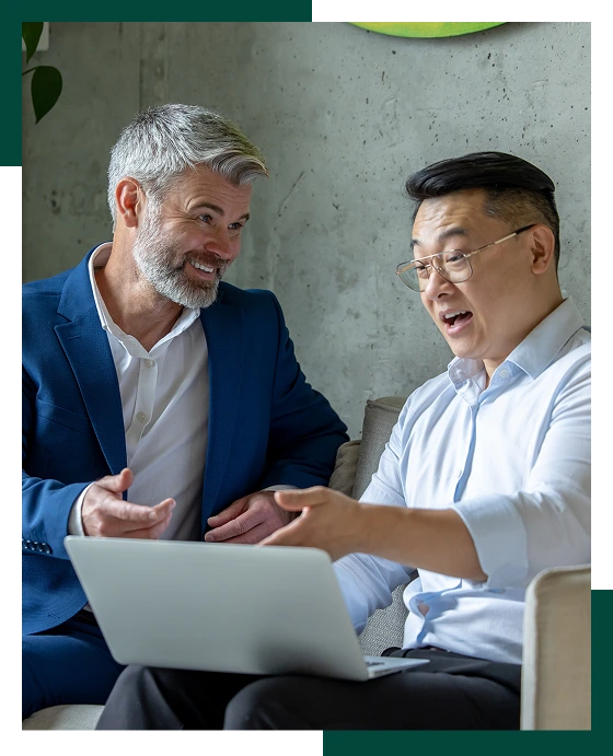 Business men sitting on sofa in modern office talking together and using laptop
